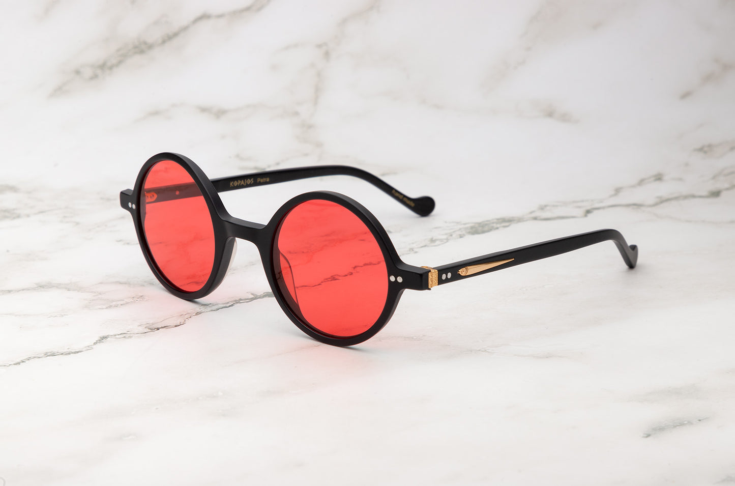 The minimalist Kopajos Petra small round sunglasses with black frame and red lenses.