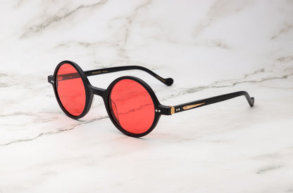 The minimalist Kopajos Petra small round sunglasses with black frame and red lenses.